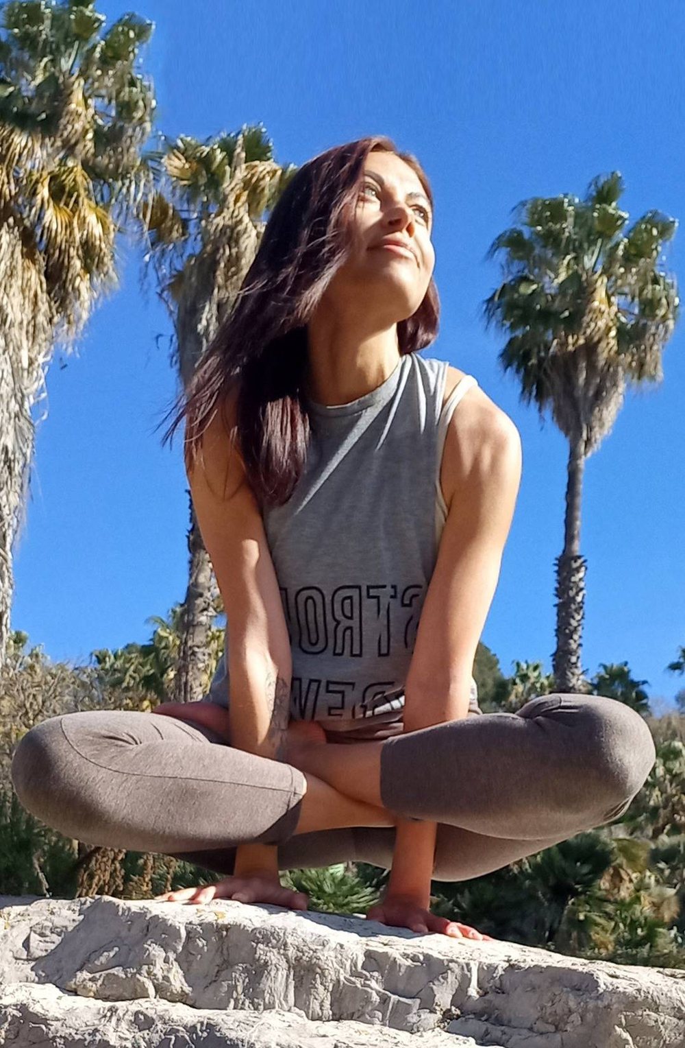 Olha Malik sitting in a yoga pose outdoors, palm trees behind her