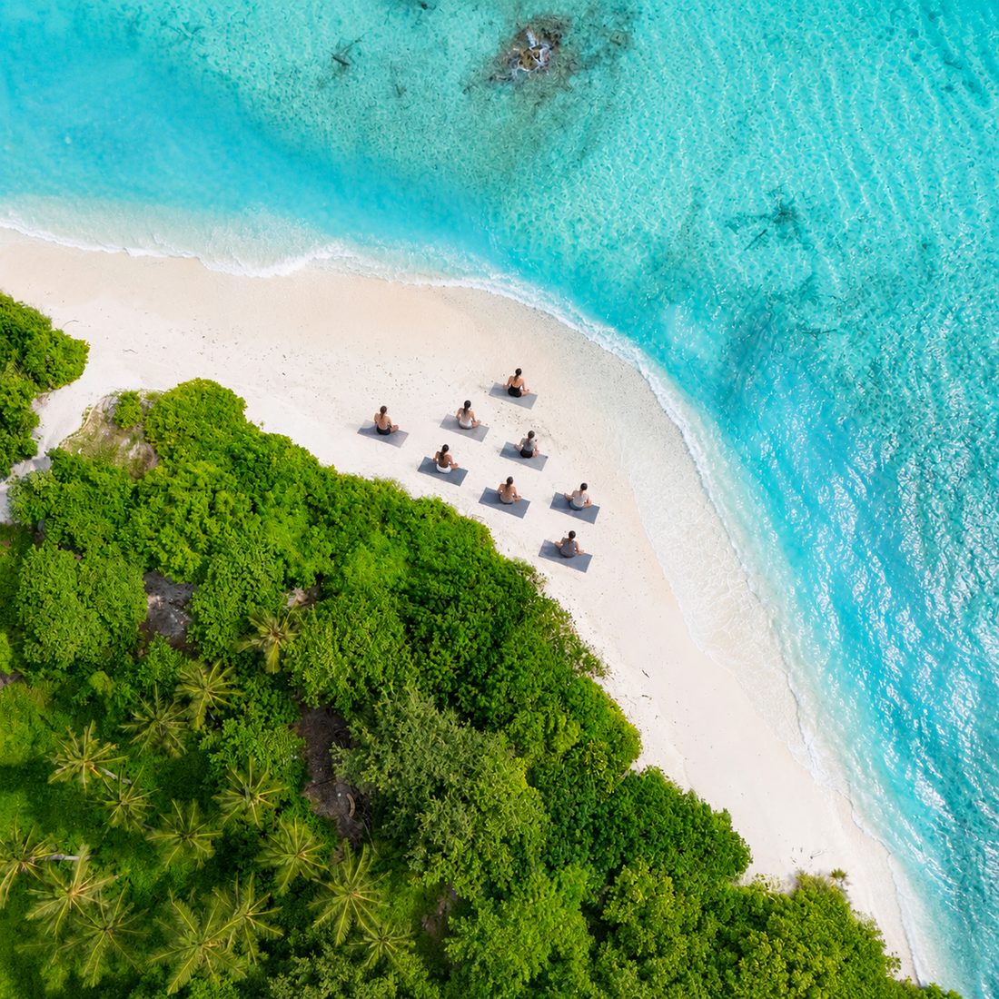 Yoga mats laid out on white sand at the edge of the lagoon, seen from above