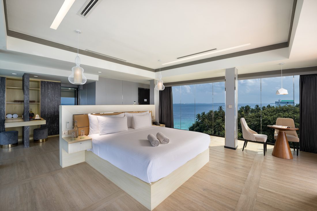 Bright bedroom with a king bed and palm trees beyond the glass